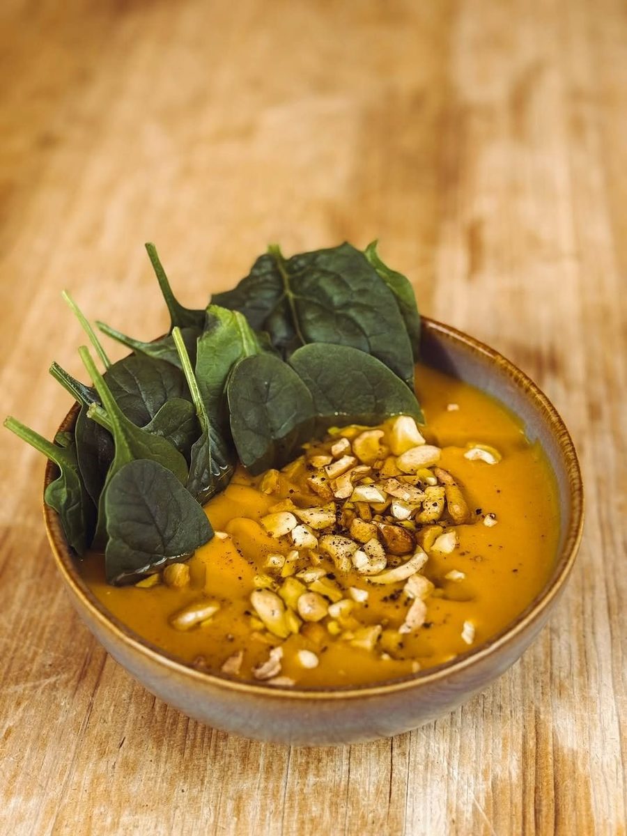 Taça de sopa cor de laranja com folhas de espinafre e sementes tostadas